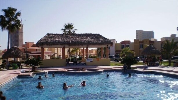 A swimming pool with multiple lanes, surrounded by palm trees and a thatched-roof pavilion. - Casita Villa Marina (Mazatlán)