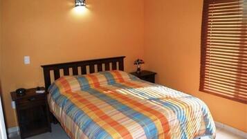 A bedroom with a bed, a nightstand, a lamp, and a window with blinds.
