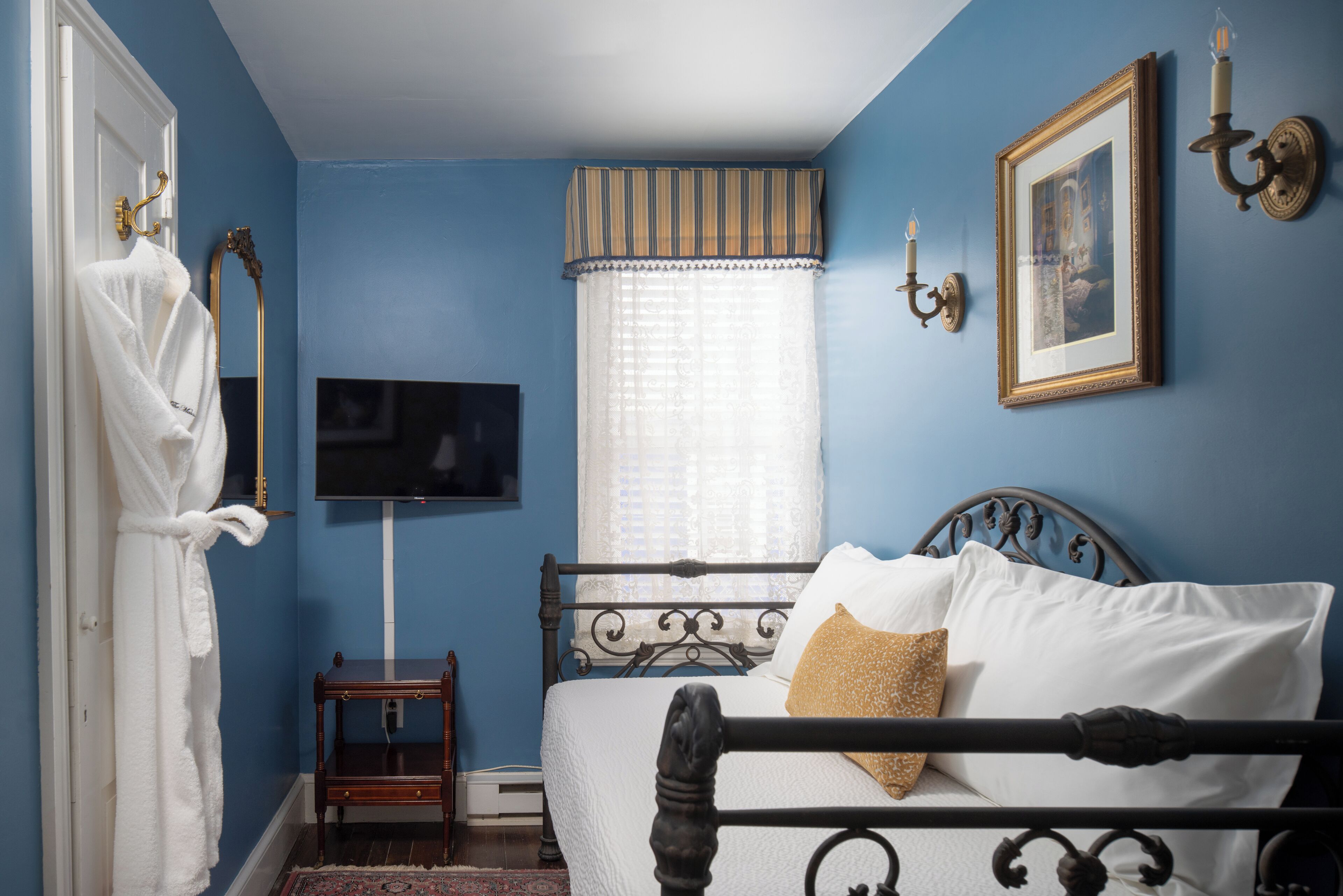 A bedroom with a bed, a TV, a window with curtains, and a painting on the wall.