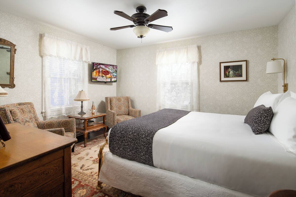 A hotel room with a large bed, a desk, a chair, a ceiling fan, and a framed picture on the wall.