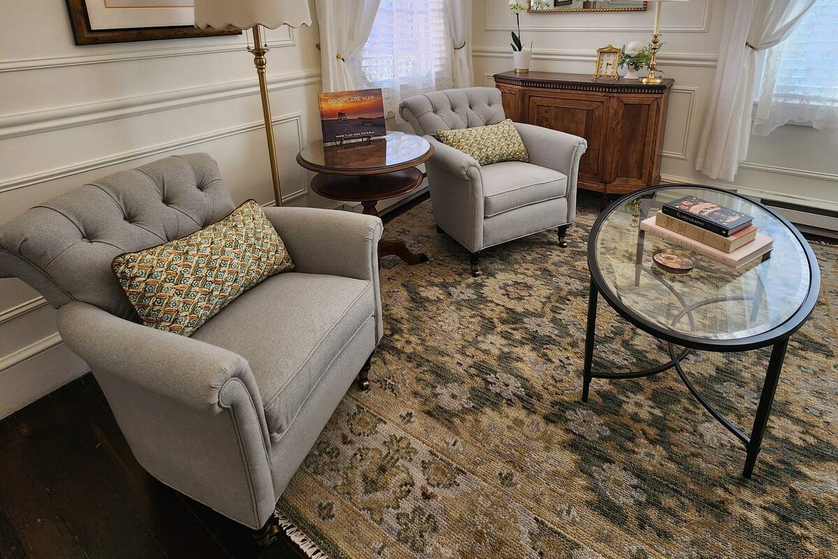 A room with a grey sofa, two armchairs, a glass coffee table, a wooden cabinet, and a large mirror.