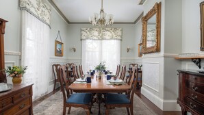 A dining room with a wooden table set for six, surrounded by chairs.