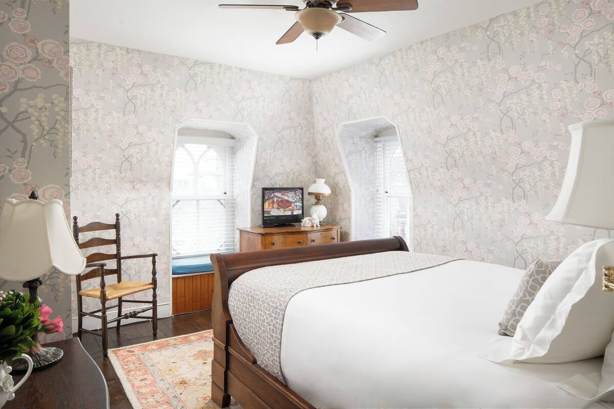 A bedroom with a bed, a wooden chair, a dresser, a television, and a ceiling fan.