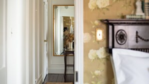 A hallway with a wooden floor, a mirror on the wall, and a door leading to another room. - The Mason Cottage (Cape May)