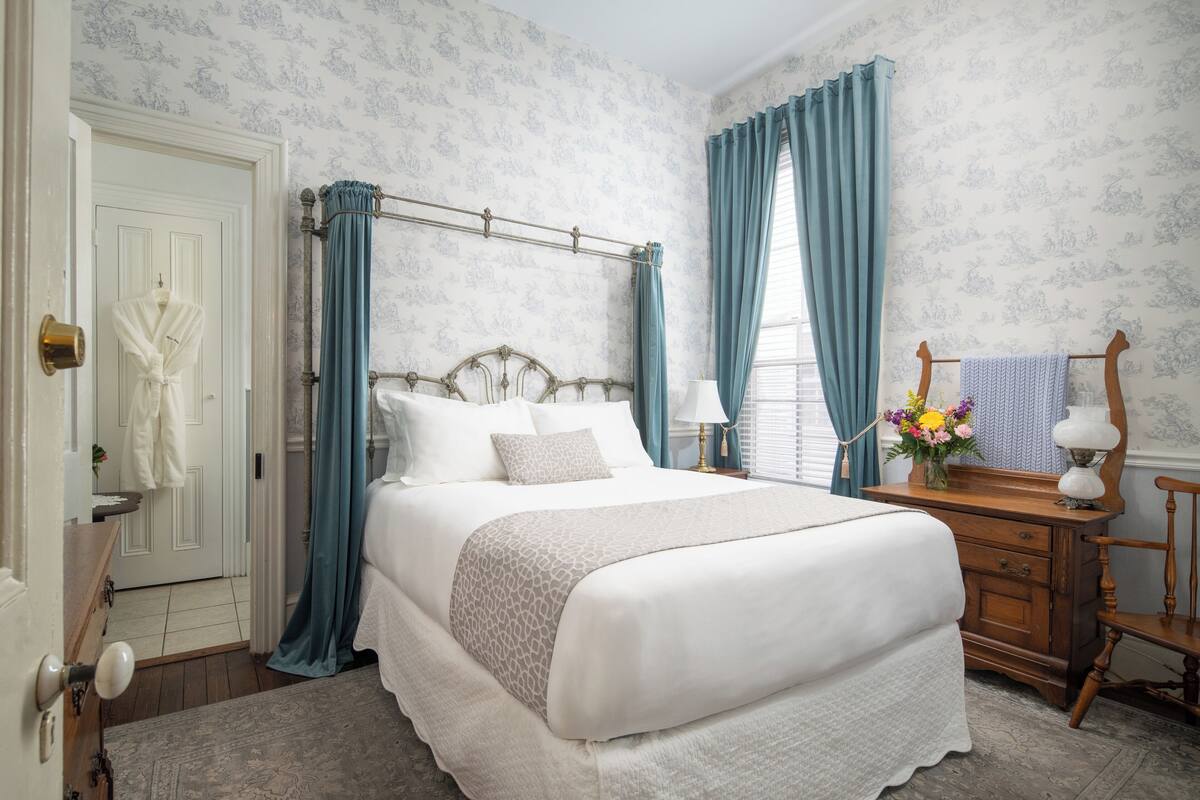 A bedroom with a four-poster bed, a wooden dresser, and a vanity with a mirror.