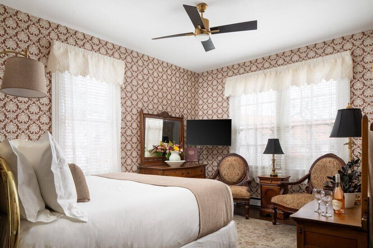 A hotel room with a bed, a desk, a chair, a television, and a ceiling fan.
