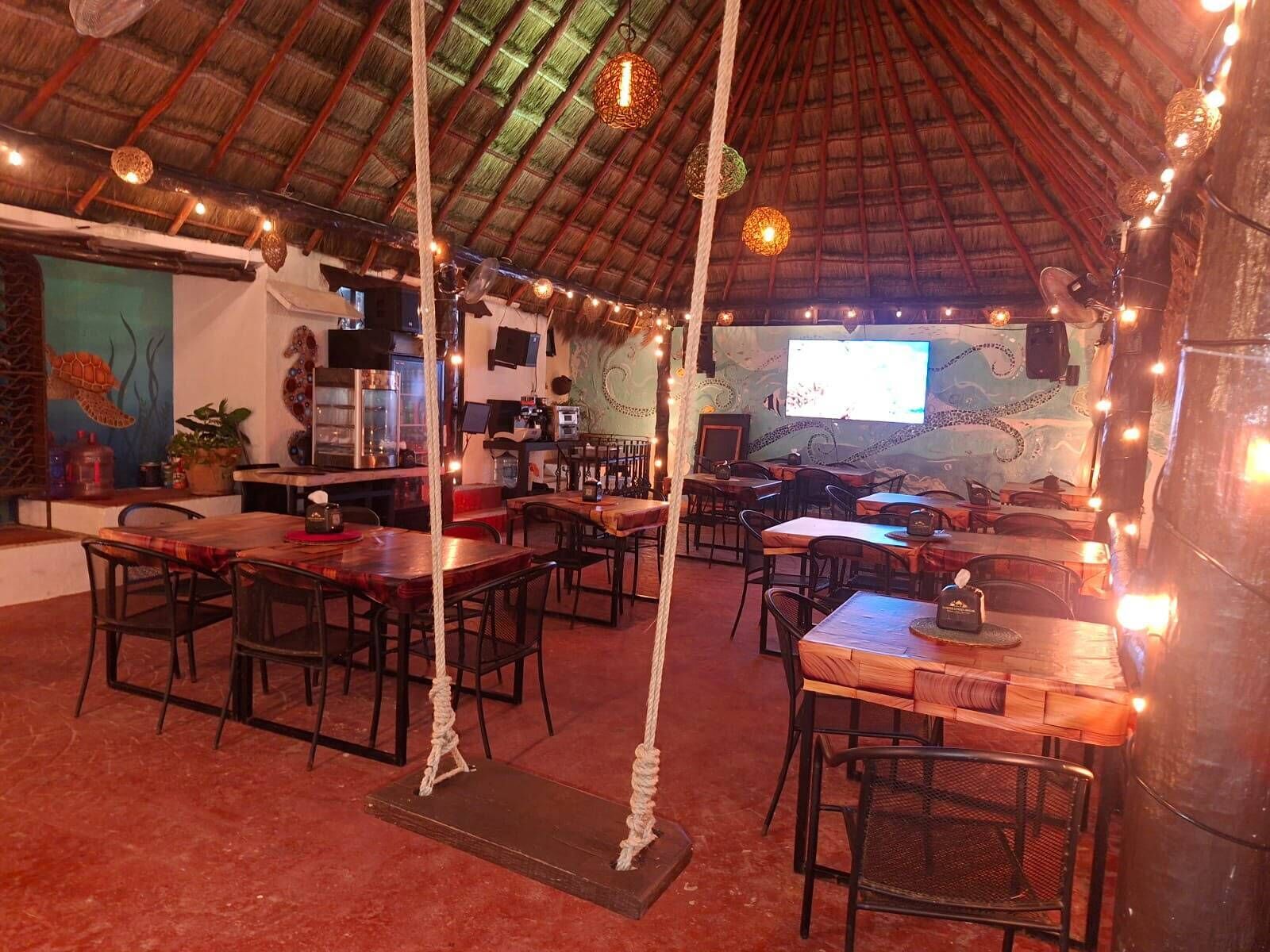 Un restaurante con techo de paja, mesas de madera y luces colgantes.
