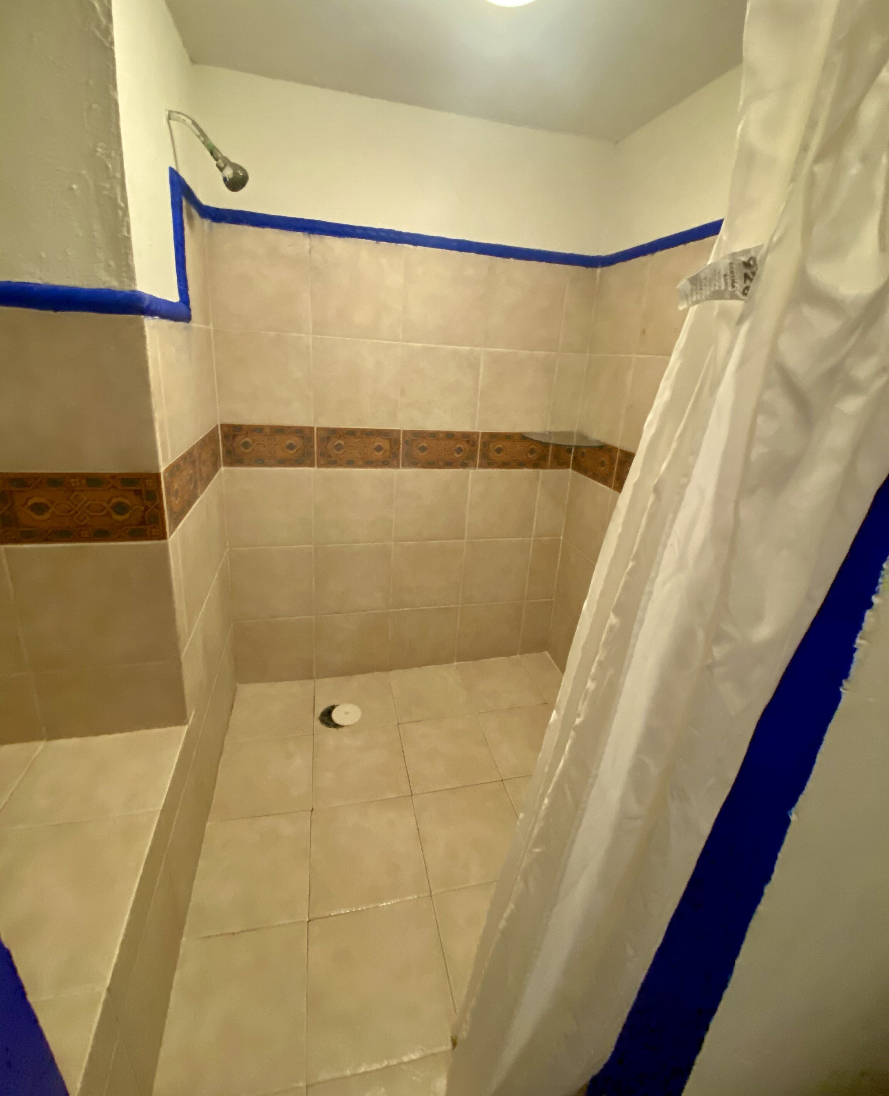 Un espace douche avec des murs carrelés, un rideau de douche et un drain.