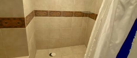 Un espace douche avec des murs carrelés, un rideau de douche et un drain.
