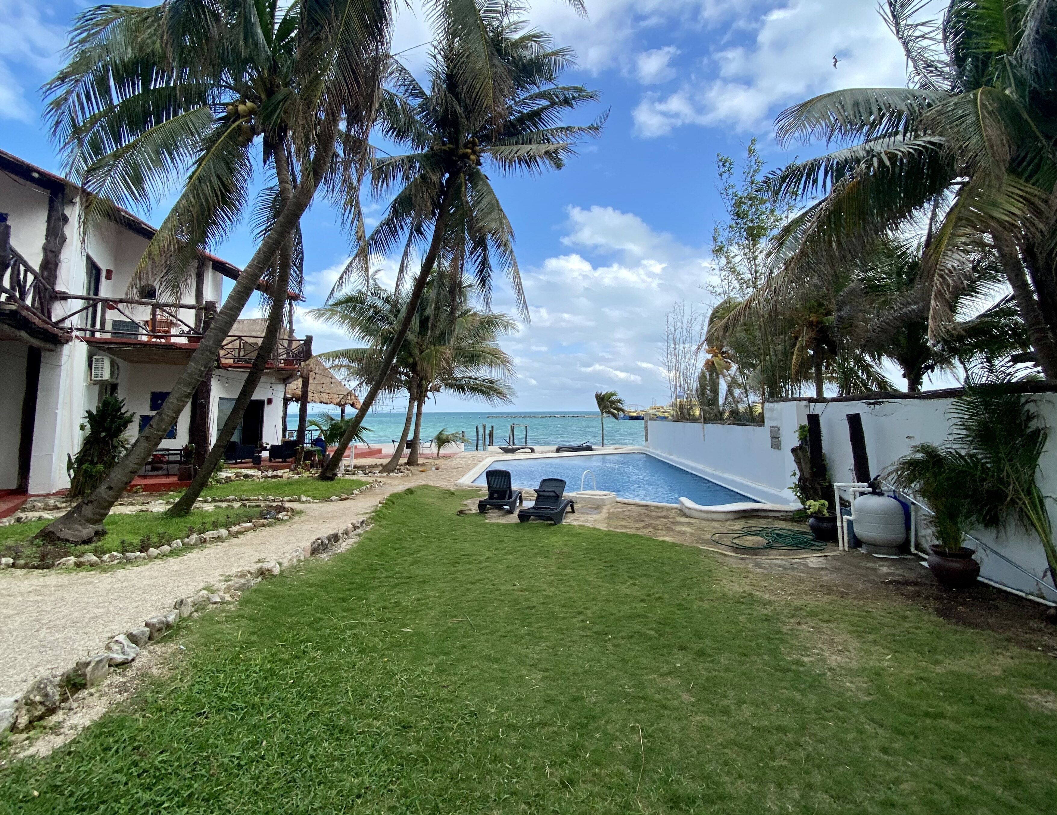 Un área de piscina con sillones reclinables, una piscina pequeña y vista al océano.
