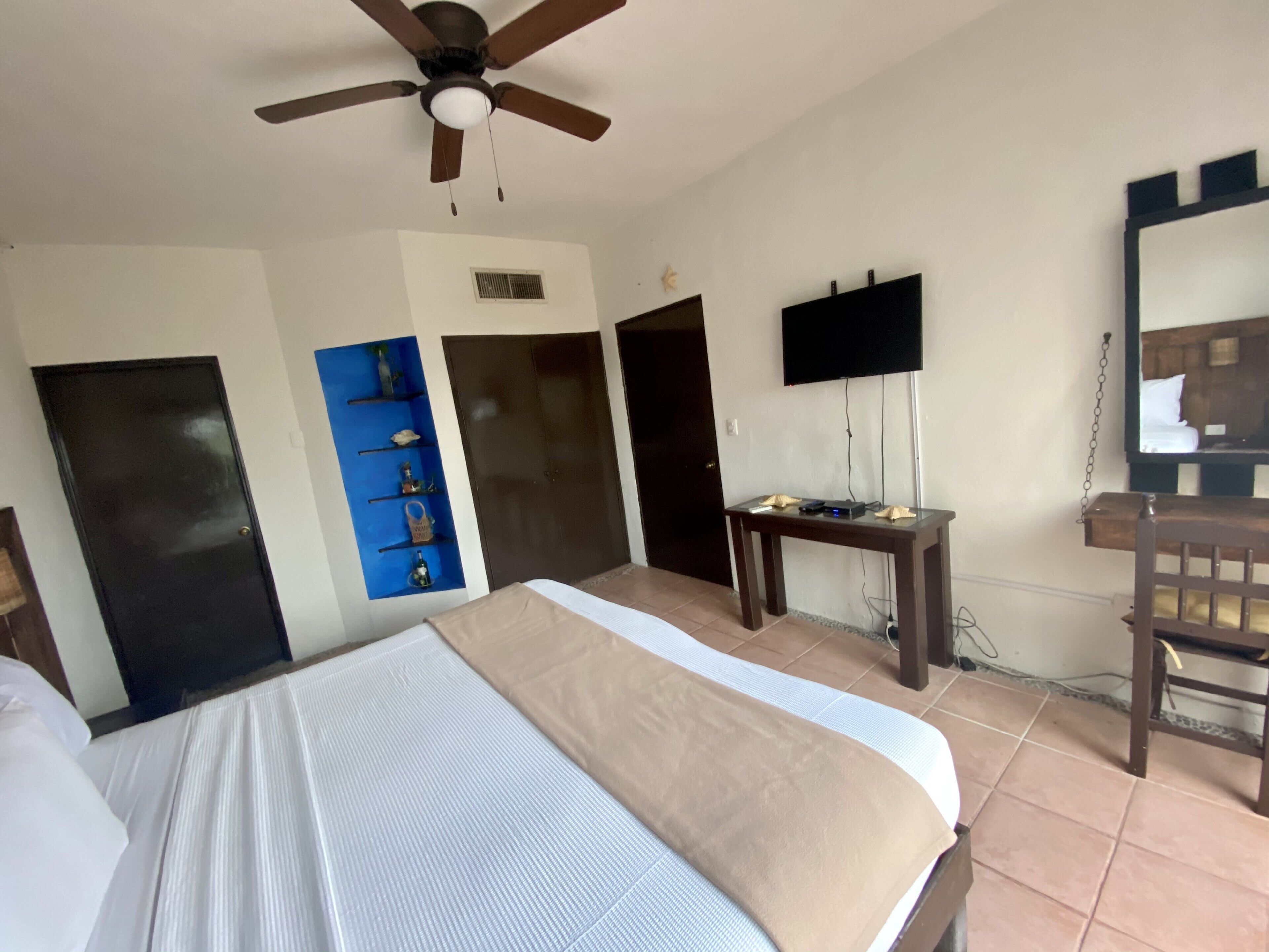 Een hotelkamer met een bed, een plafondventilator, een televisie, een bureau en een stoel.
