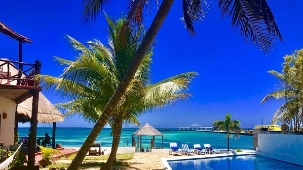 A pool area with lounge chairs, a thatched-roof structure, and a view of the ocean. - Casa Caribe Cancun (Cancun)