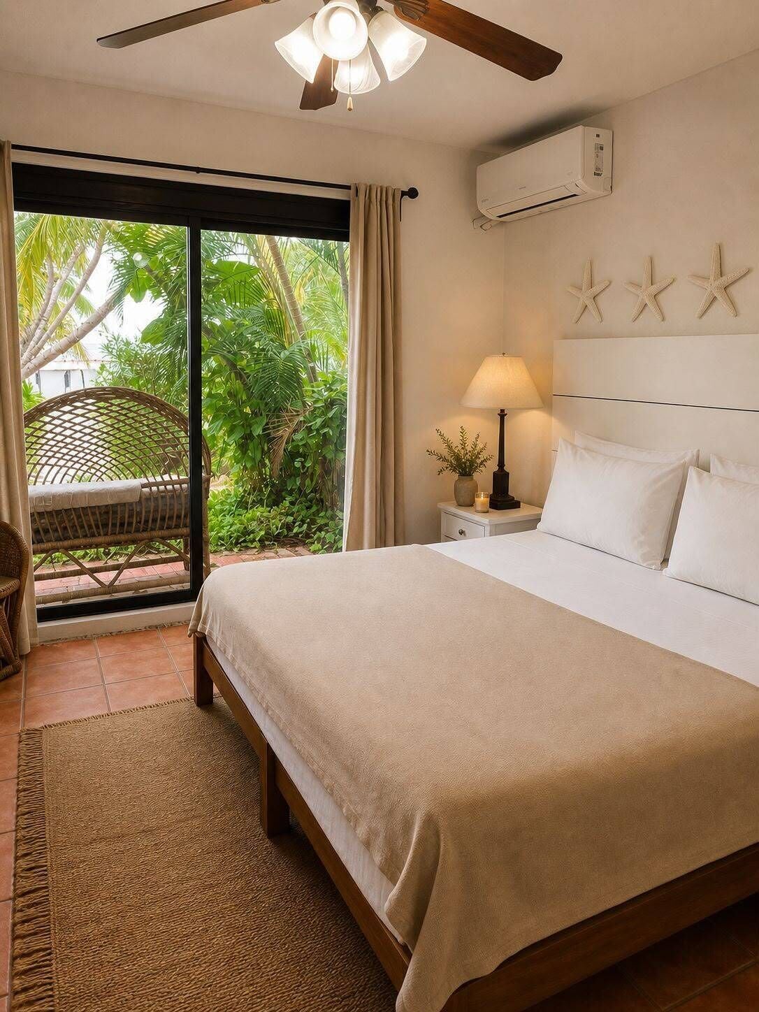 A bedroom with a bed, a nightstand, a lamp, a ceiling fan, and a view of greenery outside.