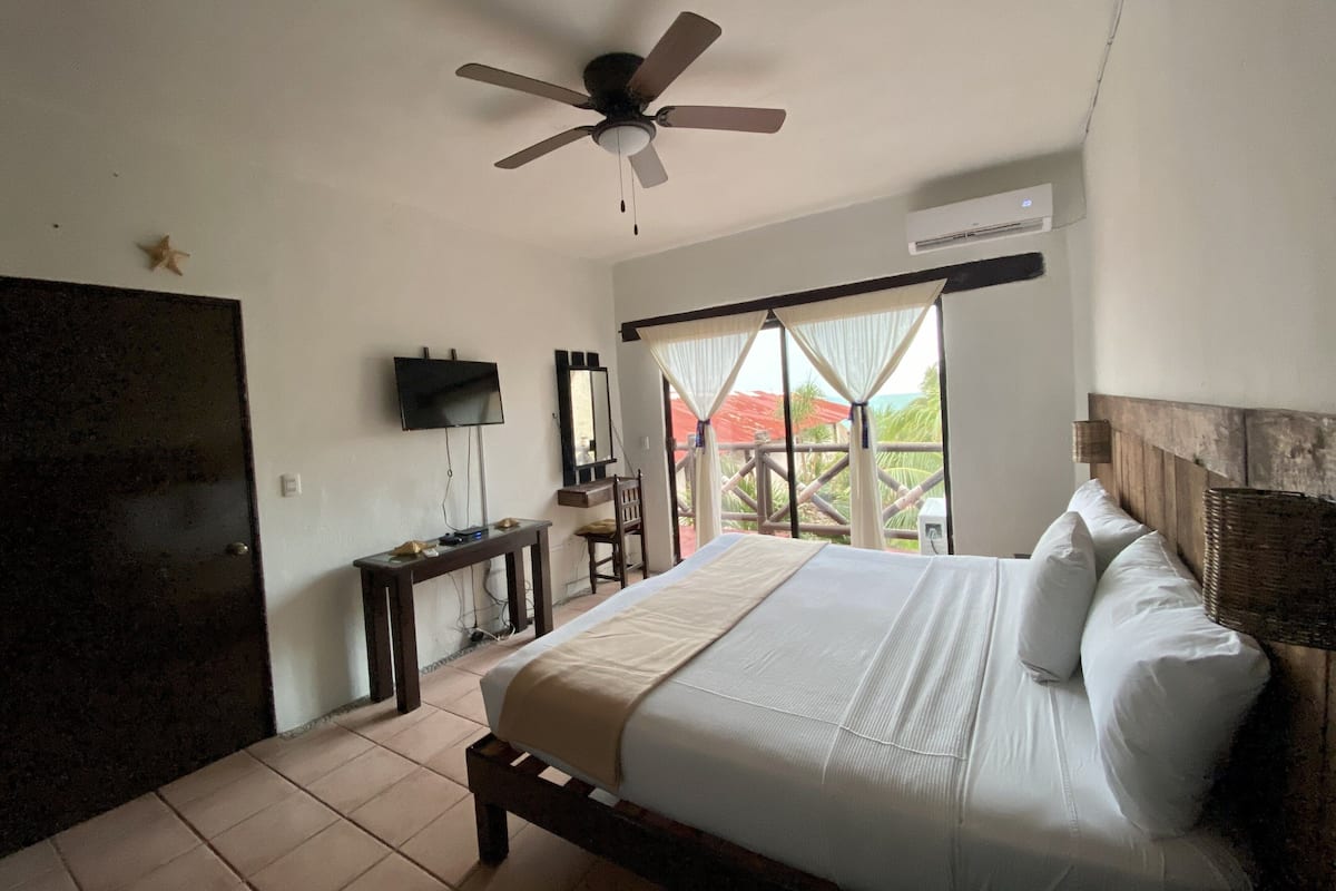 Ein Schlafzimmer mit Bett, Deckenventilator, Fernseher, Schreibtisch und einem Fenster mit Vorhängen.