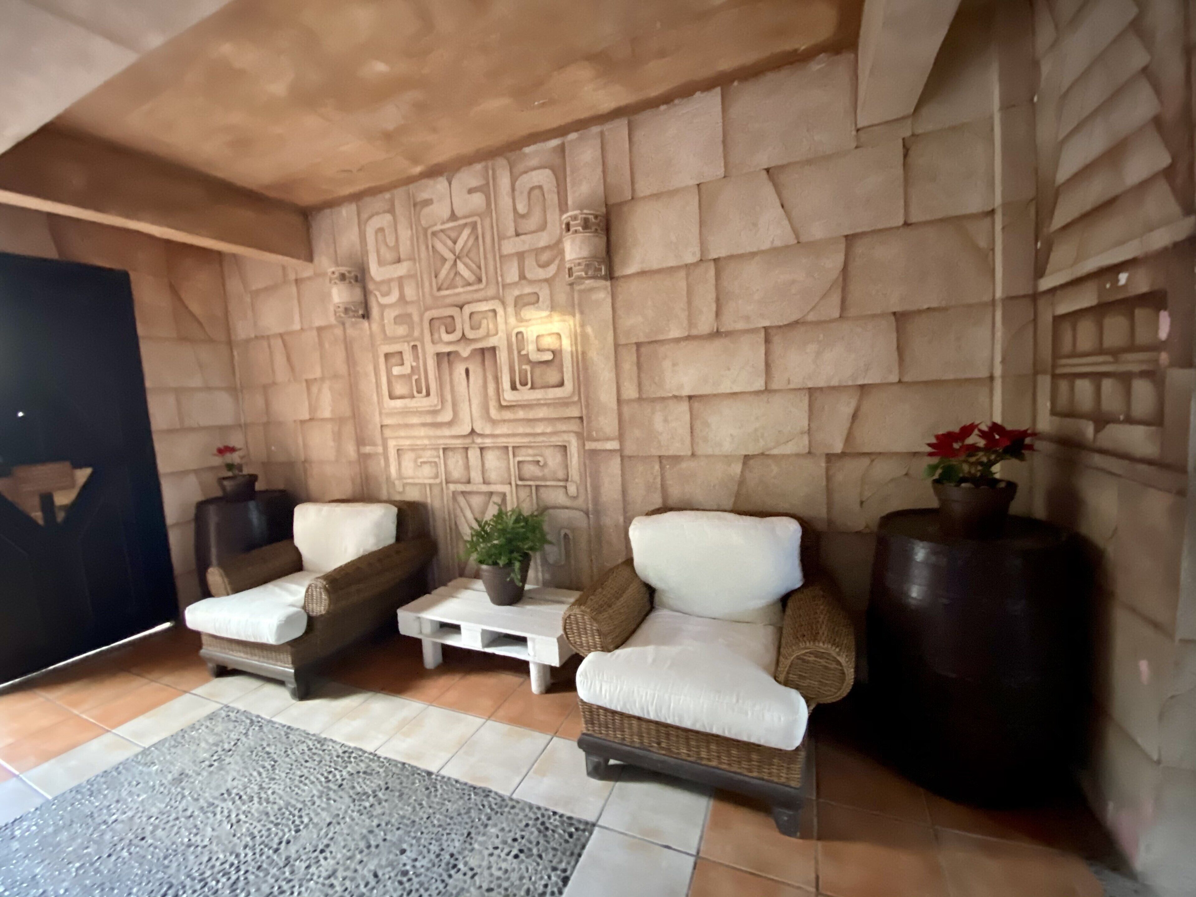 A lobby with two wicker armchairs, a small table with a plant, and a decorative wall with geometric patterns.
