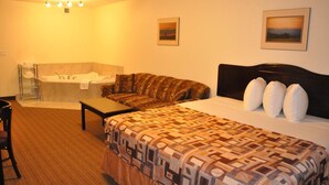 A hotel room with a bed, a sofa, a small table, a bathroom with a bathtub, and two framed pictures on the wall. - Prairie Moon Inn & Suites Unity (Unity)