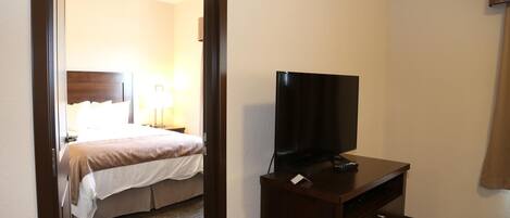 Una habitación de hotel con una cama, un televisor sobre un soporte de madera y una lámpara.