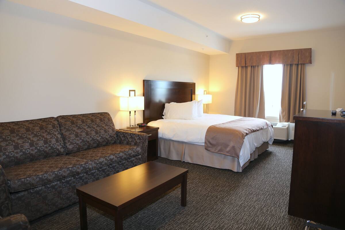 A hotel room with a bed, a sofa, a nightstand, a lamp, and a desk.