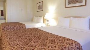 Een hotelkamer met twee bedden, een nachtkastje met een lamp, en twee ingekaderde foto's aan de muur.