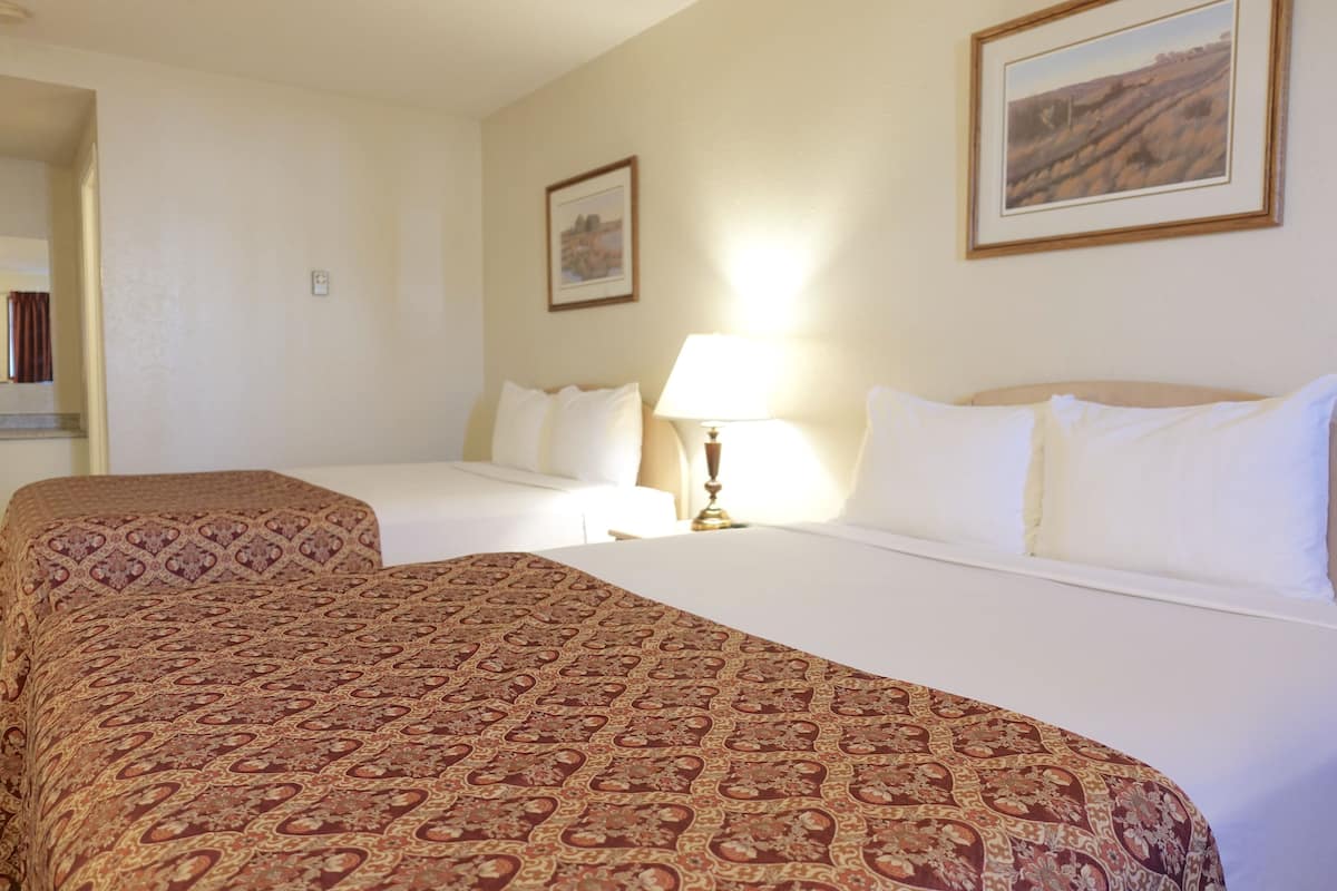 Quarto de hotel com duas camas, uma mesa de cabeceira com abajur e duas quadros na parede.