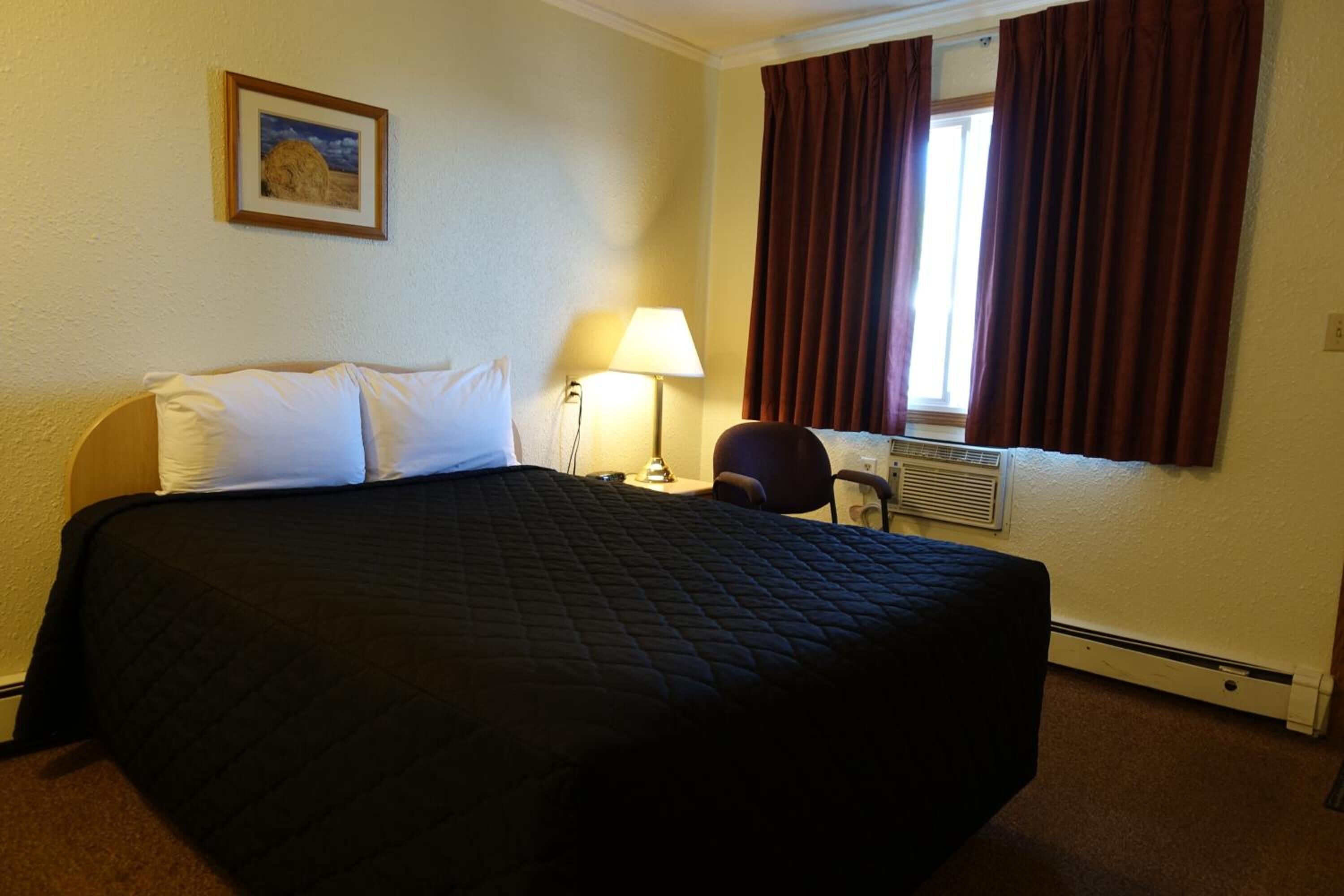 A hotel room with a large bed, a desk, a chair, a lamp, and a window with curtains.