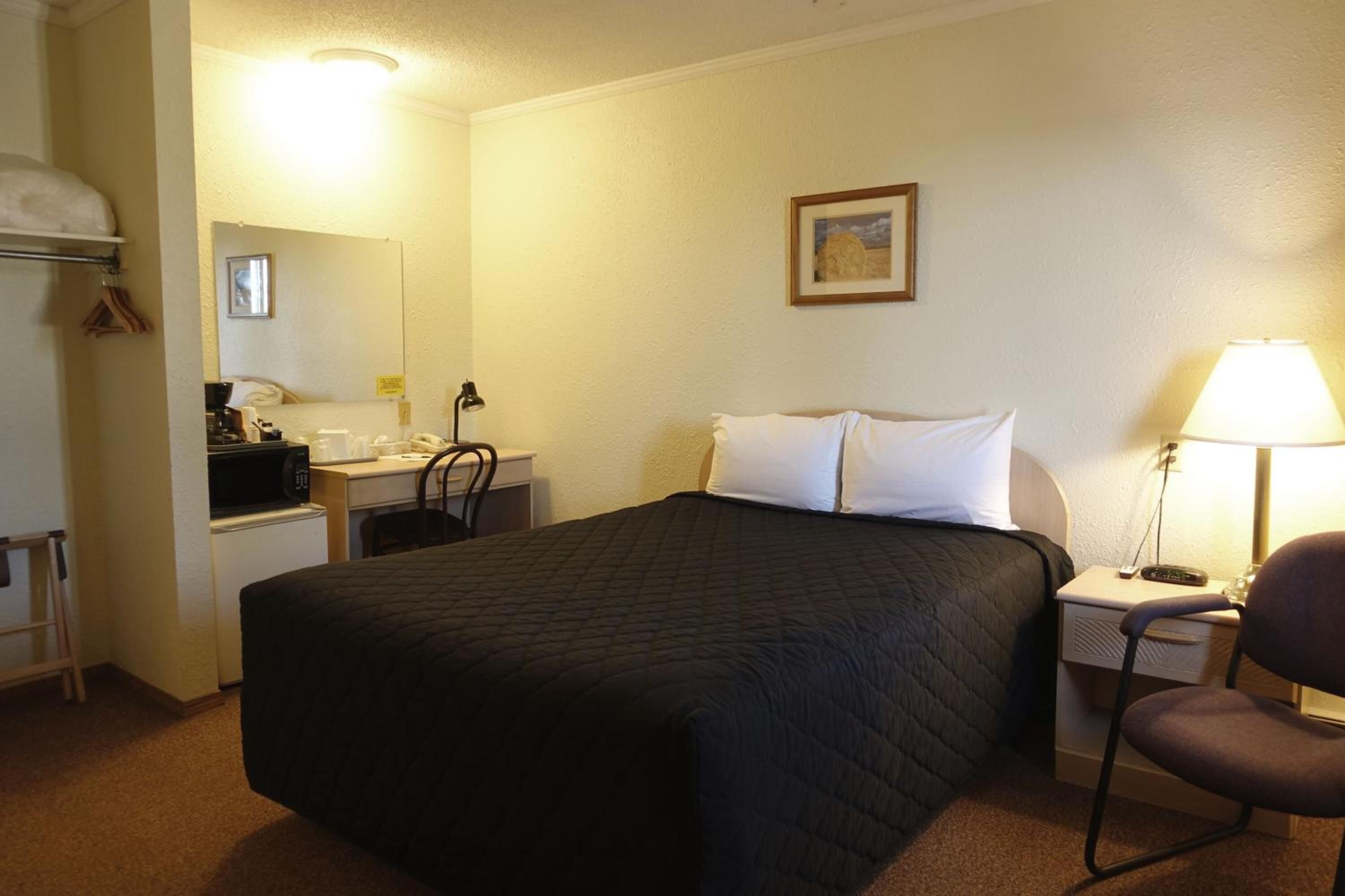Une chambre d’hôtel équipée d’un lit, d’un bureau avec une chaise, d’une lampe, d’un four à micro-ondes et d’un petit réfrigérateur.