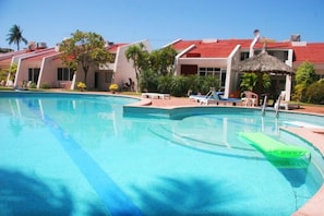 A swimming pool with lounge chairs and a thatched-roof structure. - Casa Moises (Mazatlán)