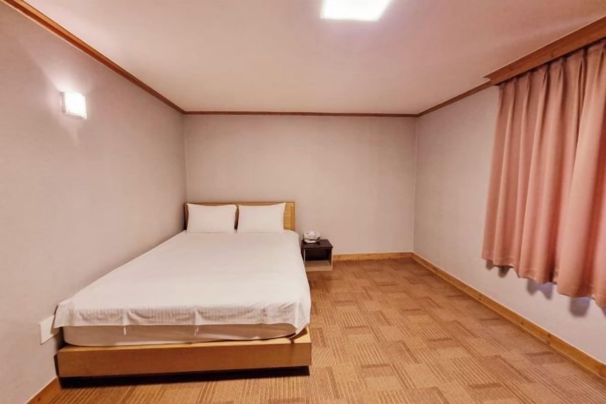 Ein Schlafzimmer mit einem Einzelbett, einem Nachttisch und einem Fenster mit Vorhängen.