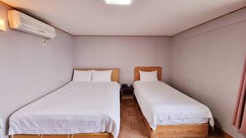 A small, clean room with two single beds, a wooden headboard, a wall-mounted air conditioner, and a small table.