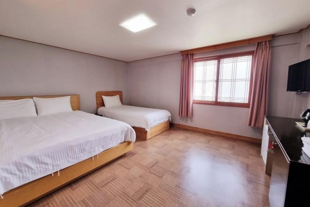 Ein Zimmer mit zwei Betten, einem Schreibtisch und einem Fenster mit Vorhängen.
