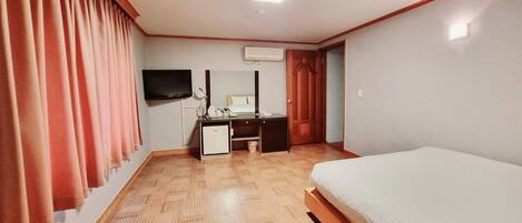 A hotel room with a bed, a desk with a chair, a television mounted on the wall, and an air conditioning unit.
