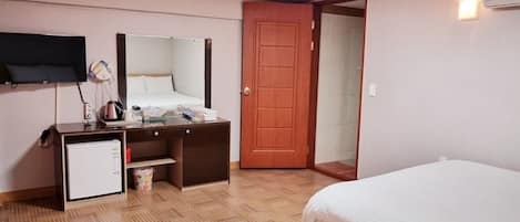 Habitación de hotel con dos camas, un escritorio con espejo, televisión y puerta que da a un baño.
