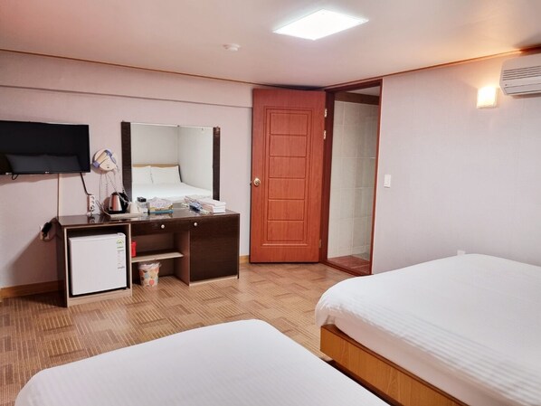 A hotel room with two beds, a desk with a mirror, a television, and a door leading to a bathroom. - Hotel G (Jeju City)