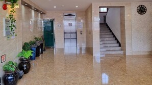 A hotel lobby with a marble floor, potted plants, an elevator, and a staircase. - Hotel G (Jeju City)