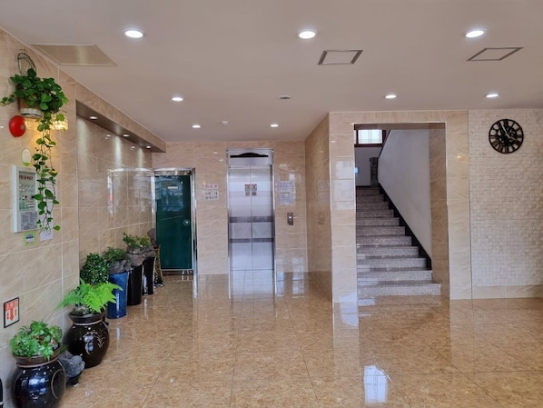 Un vestíbulo de hotel con piso de mármol, plantas en macetas, un ascensor y una escalera.