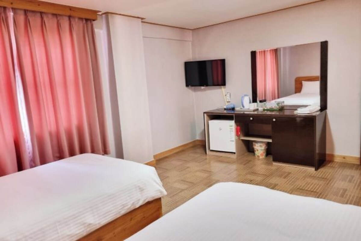 A hotel room with two beds, a desk with a computer, a TV, and a small refrigerator.