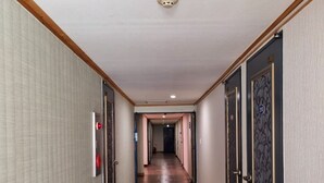 A hotel corridor with wooden trim, a textured wall, and a patterned door. - Hotel G (Jeju City)