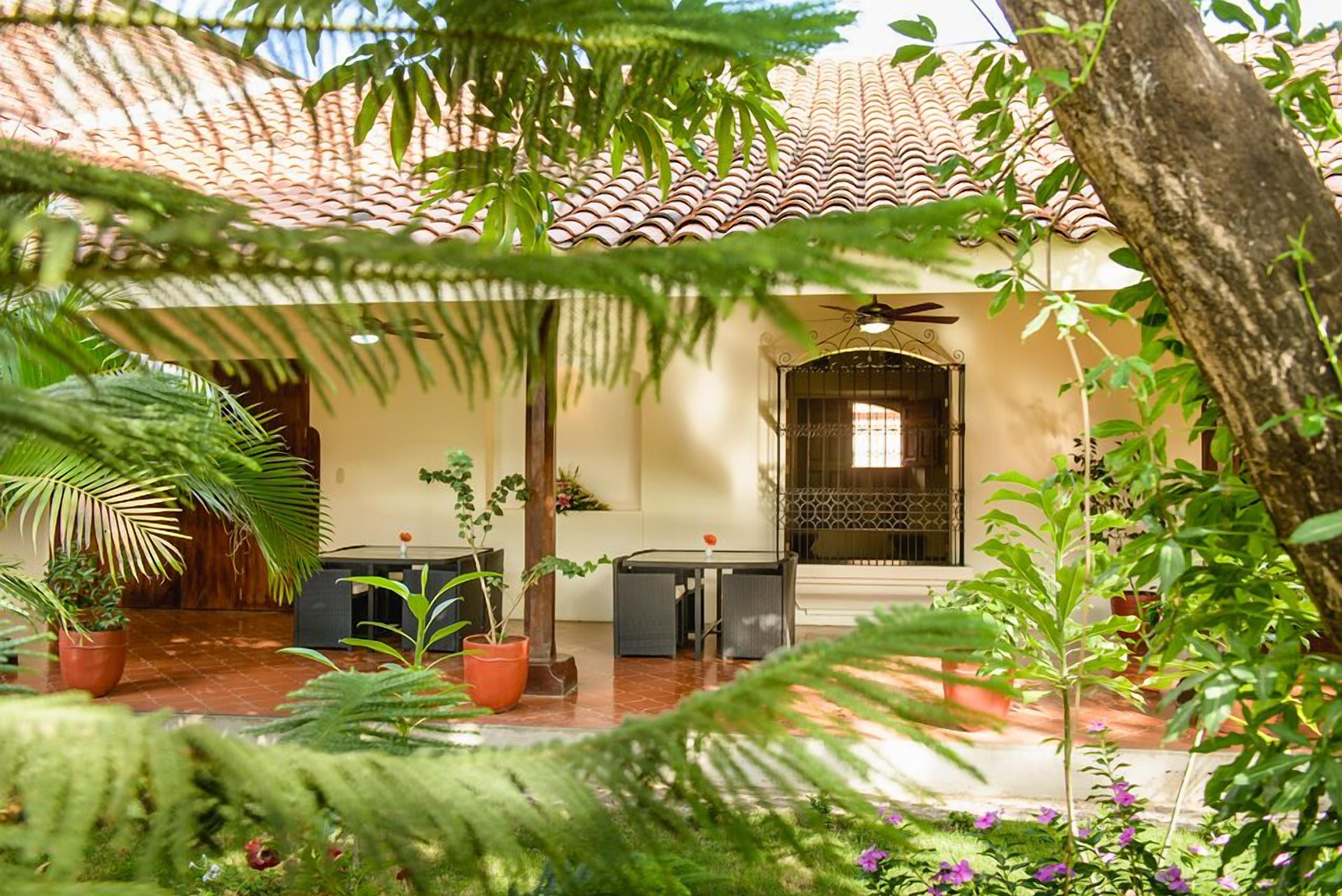 Un patio con techo de tejas, una mesa y sillas, y diversas plantas en macetas.