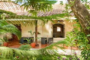 Un patio con techo de tejas, una mesa y sillas, y diversas plantas en macetas.