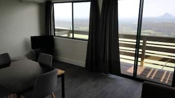 Habitación de hotel con balcón, una mesa de comedor con sillas, un televisor de pantalla plana y un amplio ventanal con cortinas.