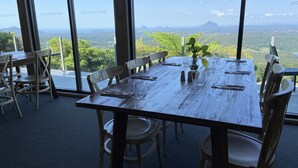 Een eethoek met een houten tafel voor zes personen, omringd door stoelen, met zicht op groen en verre bergen door grote ramen.
