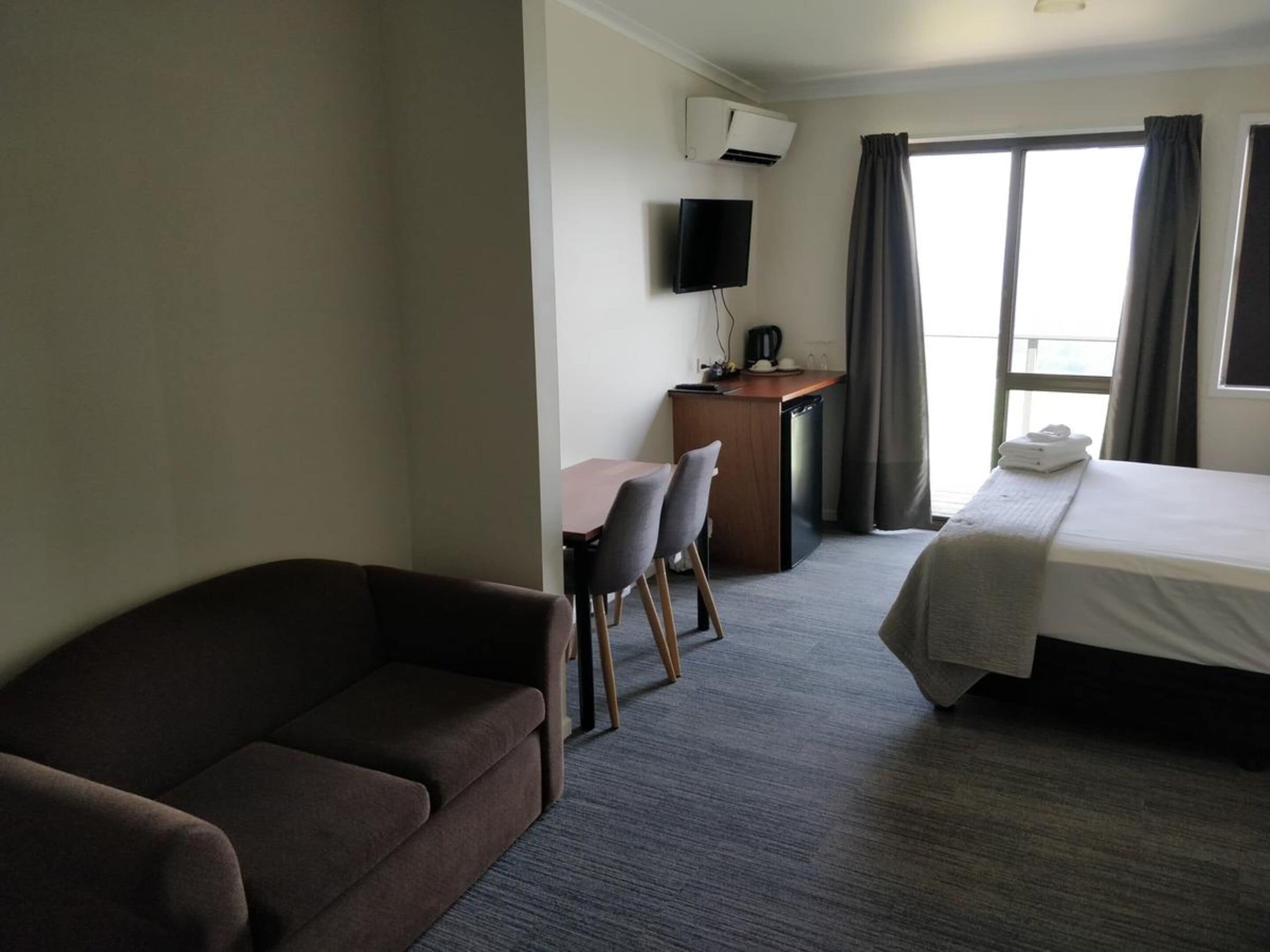 Une chambre d’hôtel comprenant un lit, un canapé, un bureau avec une télévision et une fenêtre avec des rideaux.