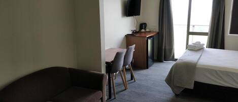 Une chambre d’hôtel comprenant un lit, un canapé, un bureau avec une télévision et une fenêtre avec des rideaux.
