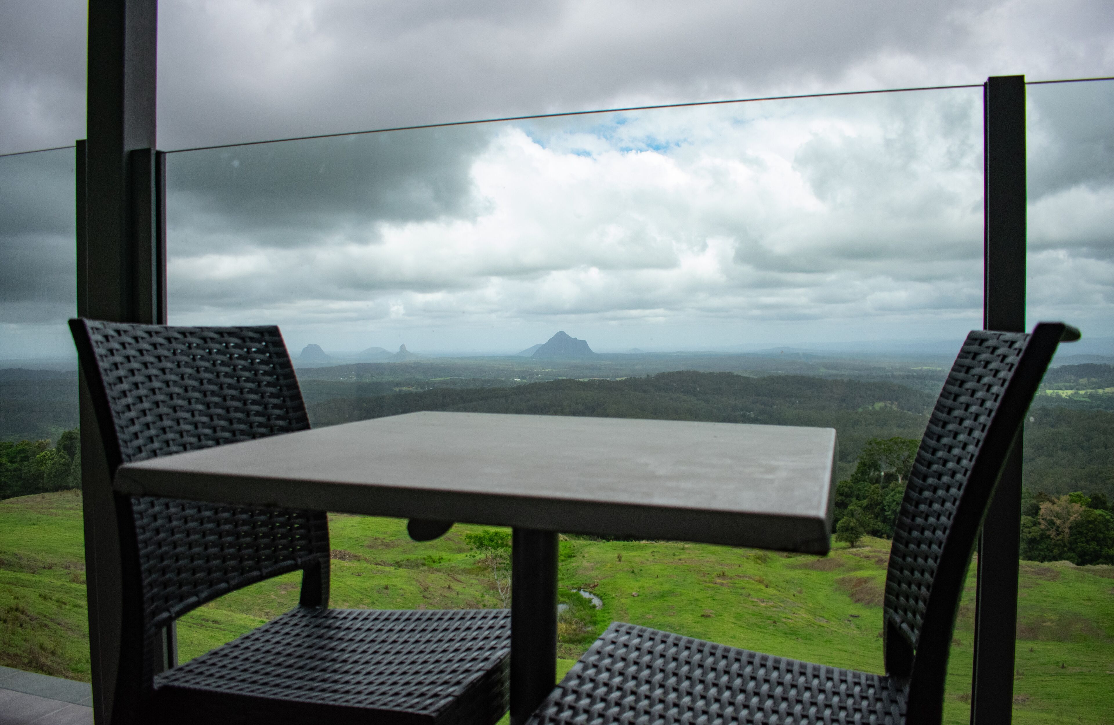 A table and two chairs with a view of a mountainous landscape through a large window.