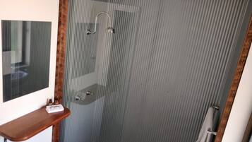 A bathroom with a shower, a mirror, and a wooden shelf.