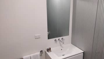 Casa de banho com lavatório branco, espelho e suporte para toalhas.