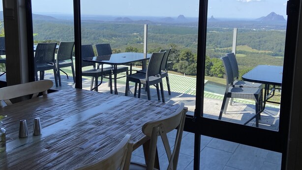 Een eethoek met een tafel en stoelen, grote ramen met uitzicht op een groen landschap en verre bergen.