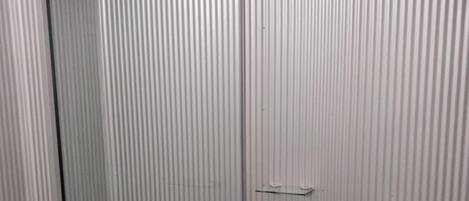 A compact bathroom with a toilet, a shower, and a small storage cabinet.