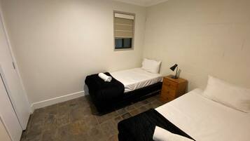 A small, clean room with two beds, a nightstand, a window, and a door.