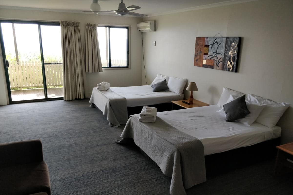 Ein Hotelzimmer mit zwei Betten, einem Deckenventilator, einem Bild an der Wand und Blick ins Freie durch das Fenster.